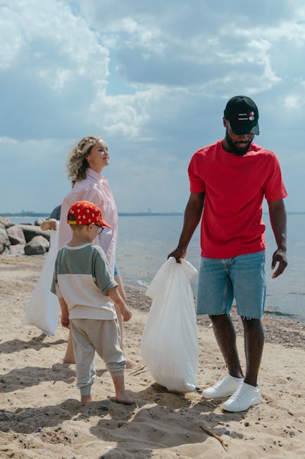 A person wearing a light blue t-shirt, black shorts, and white sneakers is collecting trash among large, irregularly shaped rocks on a rocky shoreline or outdoor area. The individual is using a grabbe