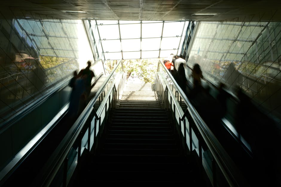 A moving train with a sleek, modern exterior painted in shades of blue and silver, captured in motion blur as it passes through a station platform. The train's windows are slightly reflective, with gl